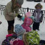 Children and a teacher in winter clothes look at the snow