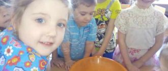 Smiling children stand next to a bowl of water with small objects floating in it